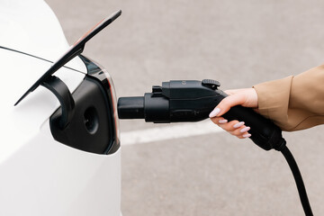 Close-up of a woman's hand charging an electric car at an outdoor charging station. Zero emission...