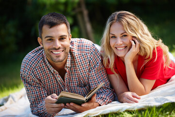 Portrait, happy couple and nature for reading book in park with green grass, together and picnic...