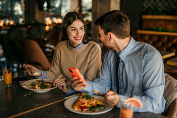 Young business colleagues having a lunch at restaurant romantic date and using smartphone