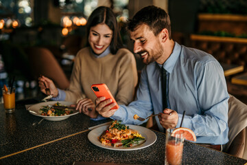 Young business colleagues having a lunch at restaurant romantic date and using smartphone