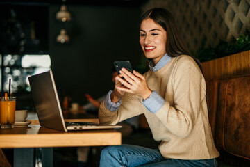 One beautiful female sitting in a bar indoors and using a laptop. Man in the background