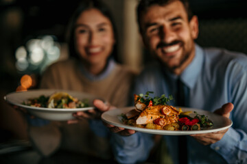Portrait of a smiling couple holding a dishes in the restaurant and smiling