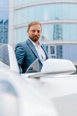 Confident business man businessman near his car on a modern street. The concept of a successful business, style and fashion, renting or selling a car.