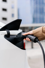 A woman turns on a zero-emission electric car at a charging station. Electric car, modern, business people.