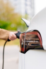 Close-up of a woman's hand charging an electric car at an outdoor charging station. Zero emission...