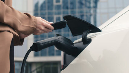 A woman turns on a zero-emission electric car at a charging station. Electric car, modern, business...
