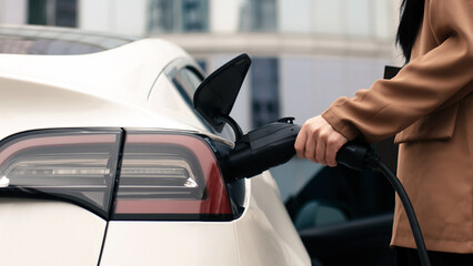 Business woman near a modern business center. A woman turns on a zero-emission electric car at a...