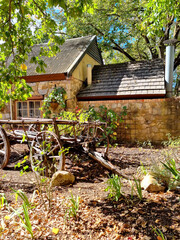 Old traditional courtyard with vintage style well near a red wooden house. Wooden farm cart with big wheels.
