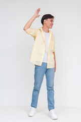 Fototapeta na wymiar Full body photo of a handsome young asian man in an unbuttoned yellow polo and white shirt and blue jeans. Boy next door vibes. Waving hi, isolated on a white background.