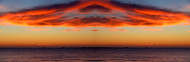 Sunset over the sea with symmetrical red clouds in the sky. Mirror image (duplicated). Clouds in the shape of a UFO