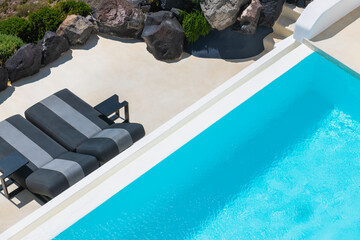 Santorini island, Greece. Luxury swimming pool with blue water and chaise lounges on the terrace.