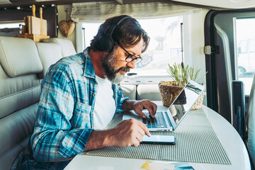 One handsome mid age man working on mobile cell phone and laptop computer inside a camper van...