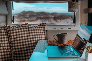 Naklejka premium Alternative office for smart working and digital nomad vanlife lifestyle. One laptop on the camper van table with nature beach amazing beautiful view. Freedom lifestyle people. Online work business