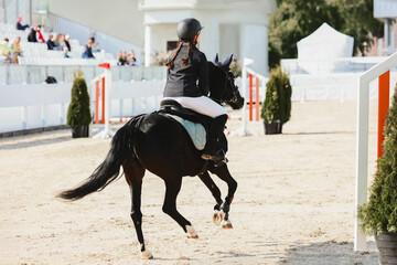 Show jumping competitions for children on ponies. A girl gallops over an obstacle on a Welsh black...