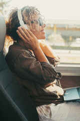 One woman listening music with headphones and computer sitting inside public bus transport enjoying...