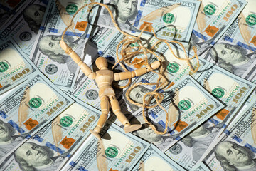 A wooden doll on a rope lies on dollars, manipulating people with money, business