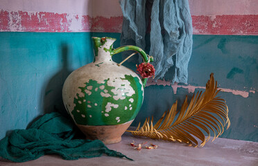 An old, peeling ceramic jug and a dried palm branch.