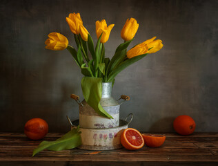 Still life with a bouquet of yellow tulips and red oranges.