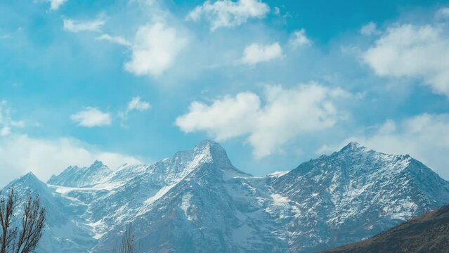 4K Time lapse of dancing clouds above the snow mountains. Winter mountain landscape. View from Keylong, Lahaul, India. Bright sunny day, cold atmosphere. Travel, trekking and holidays concept.