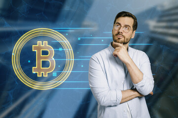 Thoughtful handsome young businessman with creative growing round bitcoin hologram on blurry city...