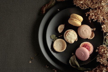 Delicious sweet colorful macaroons with dried flowers on a black plate.
