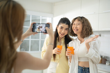 Two smiling women taking a selfie with orange drinks in a bright, modern kitchen, enjoying their...