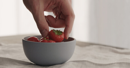 man take fresh strawberries from blue bowl on linen cloth