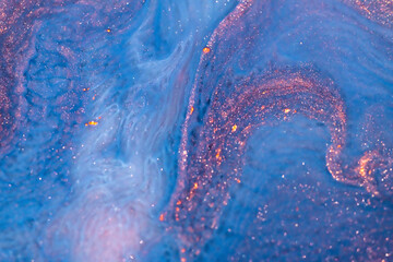 Blue and pink acrylic paints with shimmering golden glitter. Colorful liquid paint abstract background.