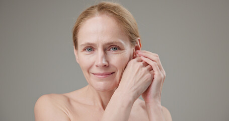 Anti age, Beauty, health and dry skin care concept - beautiful middle-aged mature Caucasian woman in her 50s touching her face skin and looking at the camera with a slight smile