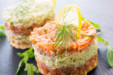 Gourmet salmon fish fruit tartar raw from salmon fillet with chopped avovado as close-up on a black...