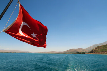 Red national flag of turkey flying, waving in the wind on the boat ride crossing Lake Van, Van Gölü to Akdamar Island, close to Van, Turkey