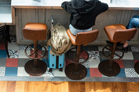 Rear view of a woman sitting in a bar stool, leaning against the wooden counter, with her trolley awaits the departure of their flight from CDG airport in Paris, France.