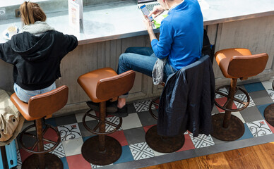 Two travelers at a bar, seated on leather stools next to a wooden counter, with their trolleys...