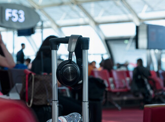 Close-up of hi-fi headphones resting in a trolley in the waiting area of the CDG airport terminal in Paris, France, in the blurry background seated strollers wait for their flight