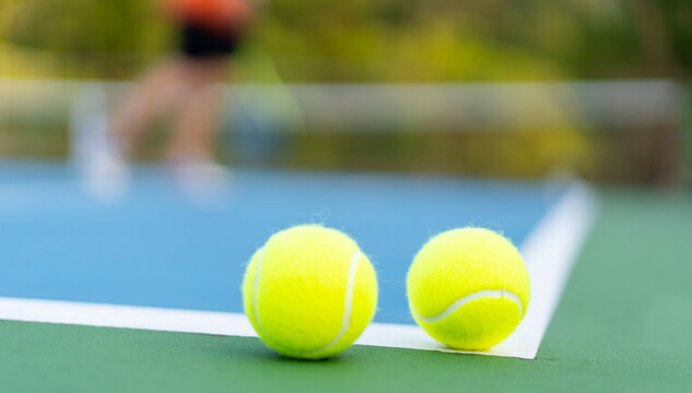 tennis balls on white line of green and blue hard court with blurred court and player as background
