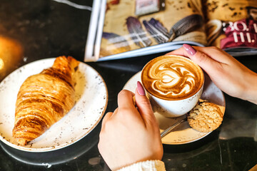 Person Holding a Cup of Coffee Next to a Croissant
