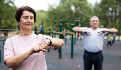 Elderly woman looking at her smart bracelet in open-air sports area