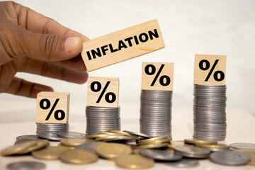 Inflation word on wooden cube with percentage icon placed on stack on coins, increase or hike in...