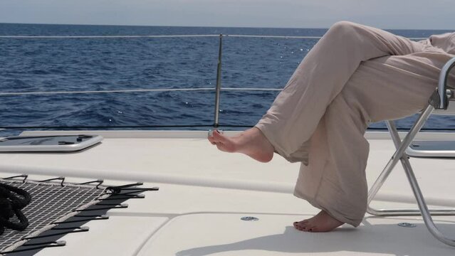 young woman wearing linen pants and knitted jamper sitting on deck of sail catamaran, freedom dream luxury vacation on yacht