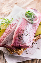 Traditional matie herring with gherkin slices and onion rings served as close-up on a rustic...