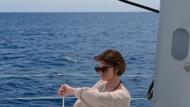 young woman wearing linen pants and knitted jamper sitting on deck of sail catamaran, freedom dream luxury vacation on yacht