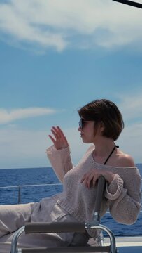 young woman wearing linen pants and knitted jamper sitting on deck of sail catamaran, freedom dream luxury vacation on yacht
