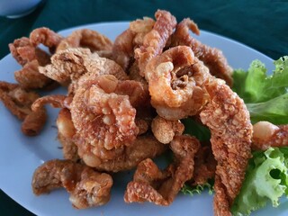 A plate piled high with golden brown fried chicken. The chicken pieces are various shapes and sizes, with a crispy batter coating. 