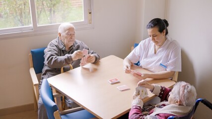 Senior people and caregiver playing cards in a nursing home