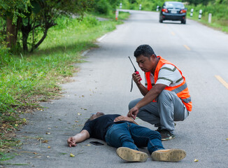 Rescue man using hand radio calling ambulance to help wounded man lying on the road