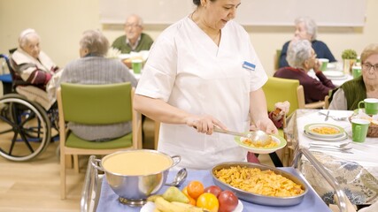 Cook serving pasta at seniors sitting in geriatric dinning room