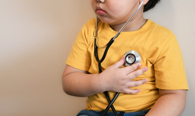 fat kid put yellow tight shirt listens to the lungs and heart with medical stethoscope. hospital...