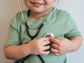 fat kid put green tight shirt listens to the lungs and heart with medical stethoscope. hospital life insurance concept, World heart health day, doctor day, world hypertension day.