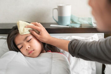 Asian mother take cool towel for reduce high fever on sick girl forehead on bed at morning time,...