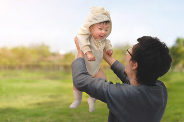 Asian father lifting toddler daughter in the air at public park, Happy family concept